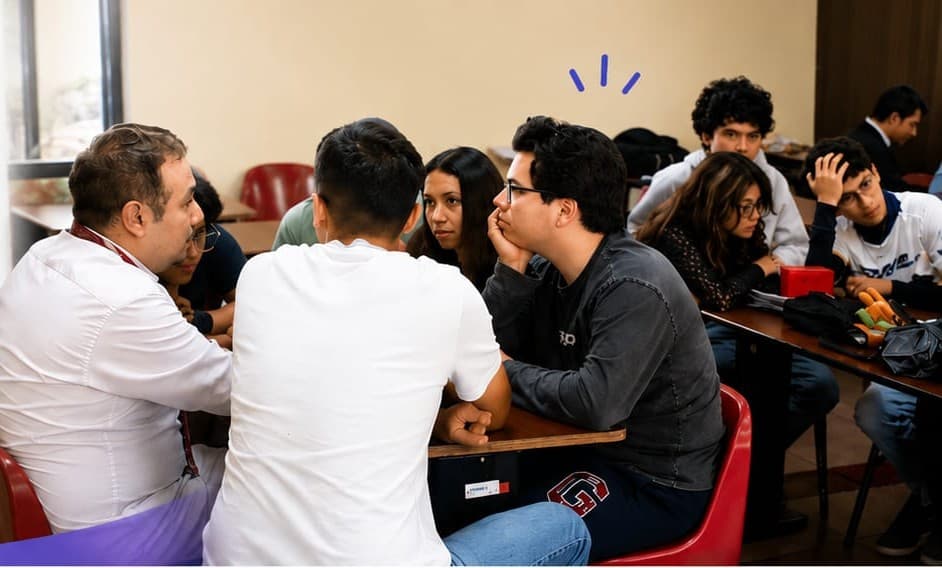 Alumnos conversando en equipos dentro de un salón de clases